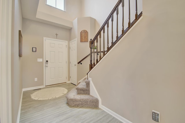 foyer featuring stairway, wood finished floors, a towering ceiling, and baseboards