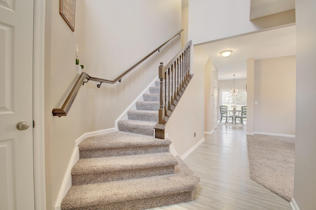 stairway featuring an inviting chandelier, wood finished floors, and baseboards