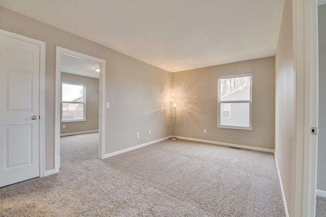 spare room featuring carpet floors, plenty of natural light, and baseboards