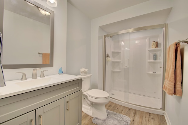 bathroom featuring toilet, a stall shower, wood finished floors, and vanity