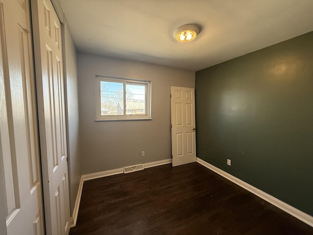 unfurnished bedroom featuring dark wood-style floors, visible vents, and baseboards