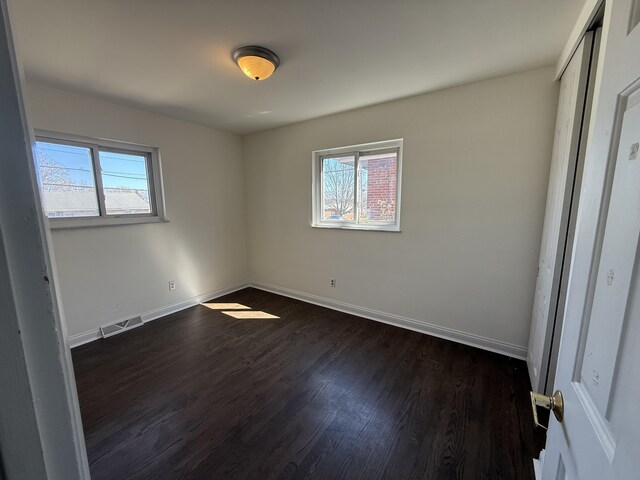 unfurnished bedroom featuring visible vents, multiple windows, dark wood-type flooring, and baseboards