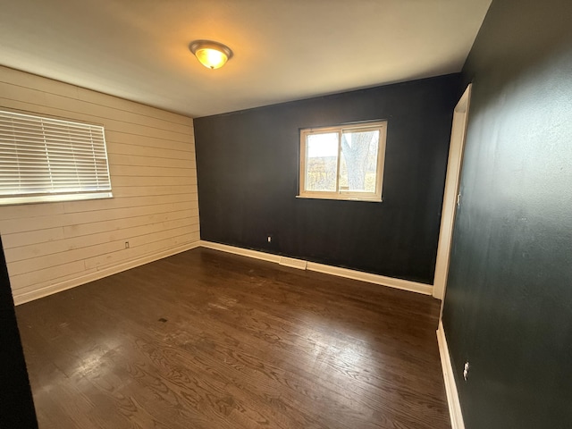 unfurnished room with dark wood finished floors, wooden walls, and baseboards