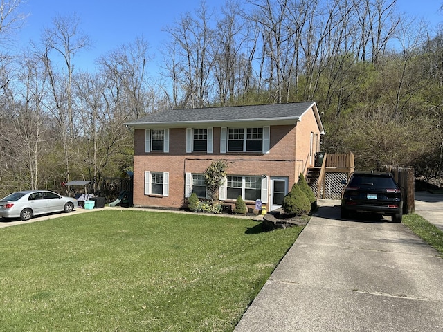 view of front facade featuring stairs, a front yard, brick siding, and driveway