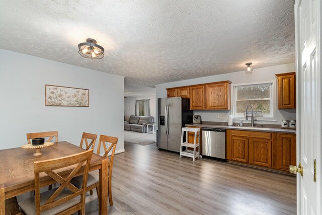 kitchen featuring a sink, stainless steel appliances, light wood-style floors, a textured ceiling, and brown cabinets