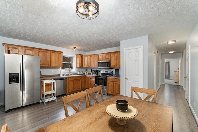 kitchen featuring a sink, a textured ceiling, wood finished floors, stainless steel appliances, and brown cabinetry