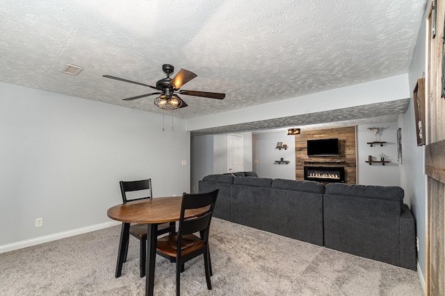 carpeted dining room with a ceiling fan, baseboards, visible vents, a warm lit fireplace, and a textured ceiling