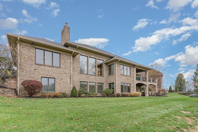 rear view of property featuring a yard, brick siding, a balcony, and a chimney