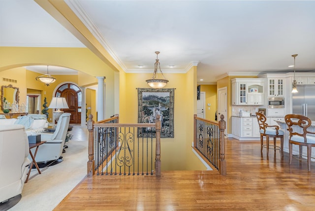 corridor with visible vents, decorative columns, an upstairs landing, light wood-style floors, and arched walkways