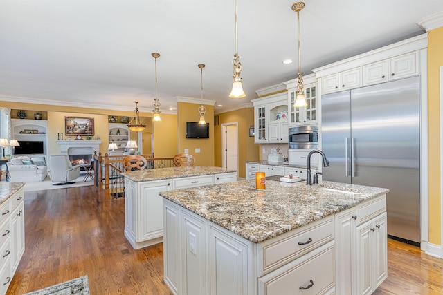 kitchen featuring a center island with sink, a warm lit fireplace, wood finished floors, open floor plan, and built in appliances