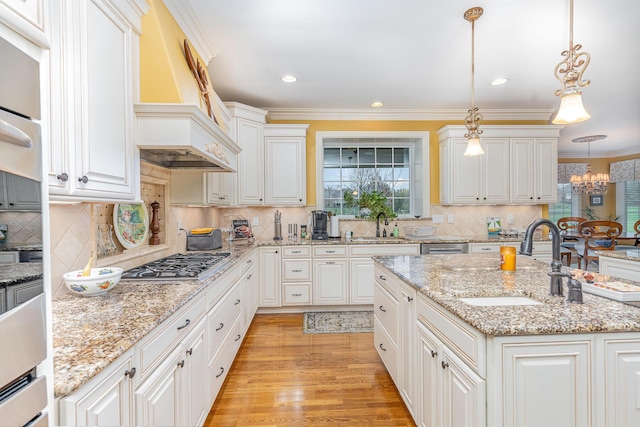 kitchen with a sink, custom exhaust hood, ornamental molding, and stainless steel gas cooktop