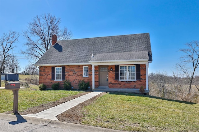 view of front of house with a shingled roof, a front lawn, brick siding, and a chimney