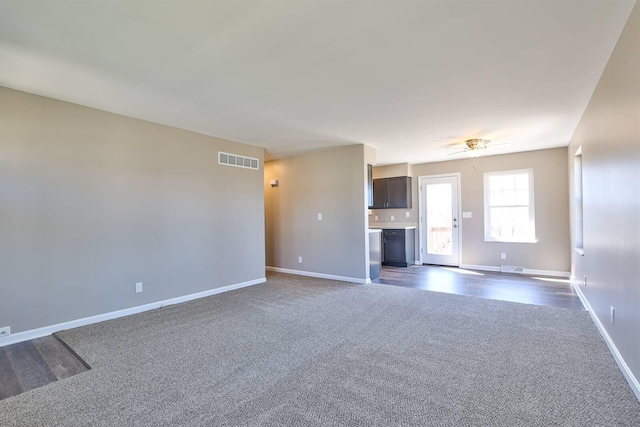 unfurnished living room with visible vents, ceiling fan, dark carpet, and baseboards