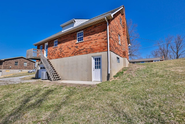 back of house featuring a yard, brick siding, and stairs