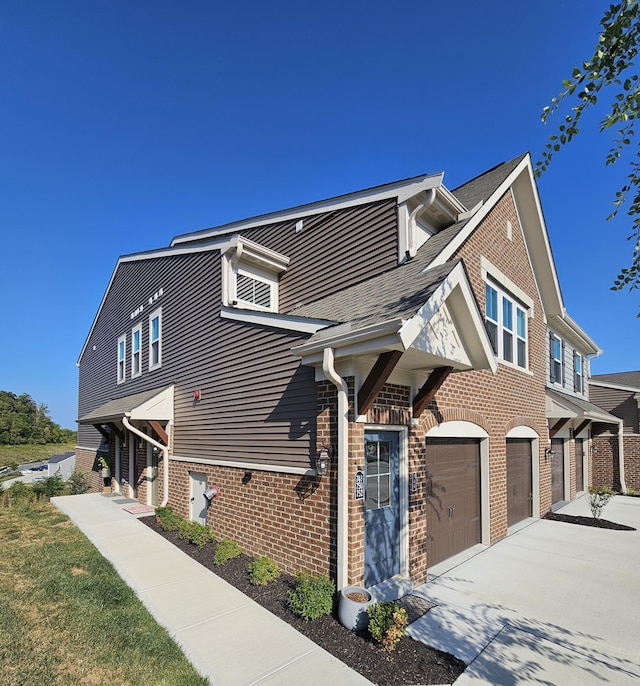 view of front of home featuring driveway, brick siding, an attached garage, and a shingled roof