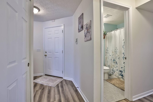 hallway with visible vents, a textured ceiling, baseboards, and wood finished floors