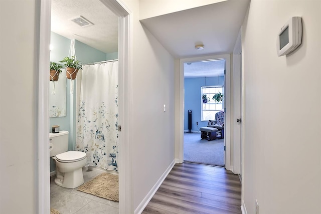 hall with wood finished floors, baseboards, and visible vents