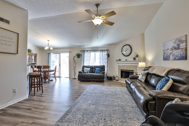 living room with wood finished floors, visible vents, vaulted ceiling, a textured ceiling, and a tiled fireplace