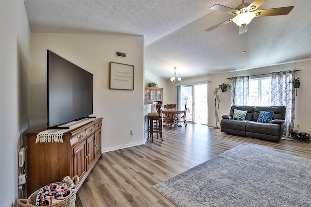 living room with visible vents, light wood finished floors, lofted ceiling, a textured ceiling, and ceiling fan with notable chandelier