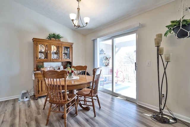 dining room featuring light wood-style floors, lofted ceiling, a notable chandelier, and baseboards