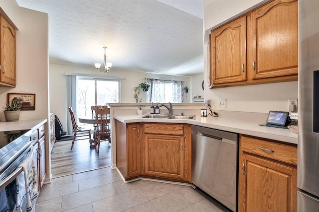 kitchen featuring a peninsula, a sink, light countertops, appliances with stainless steel finishes, and brown cabinets