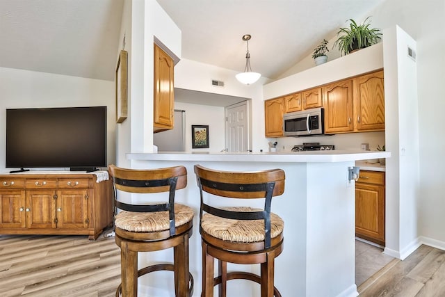 kitchen featuring stainless steel microwave, visible vents, a kitchen bar, light countertops, and lofted ceiling