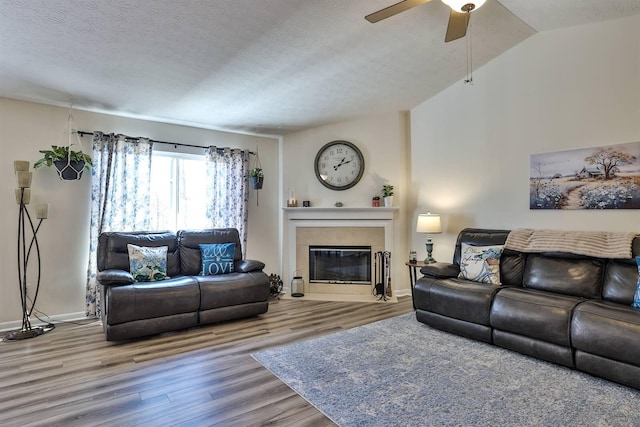 living area featuring ceiling fan, a fireplace with flush hearth, vaulted ceiling, wood finished floors, and a textured ceiling