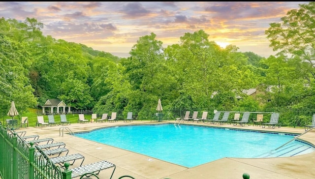 pool at dusk featuring a patio, a community pool, and fence