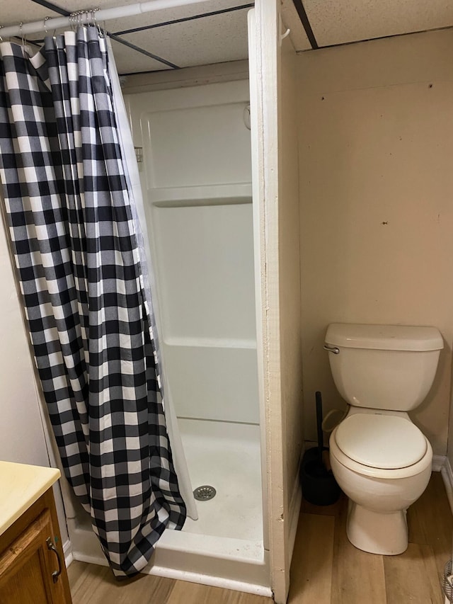 bathroom featuring vanity, wood finished floors, a shower stall, a paneled ceiling, and toilet