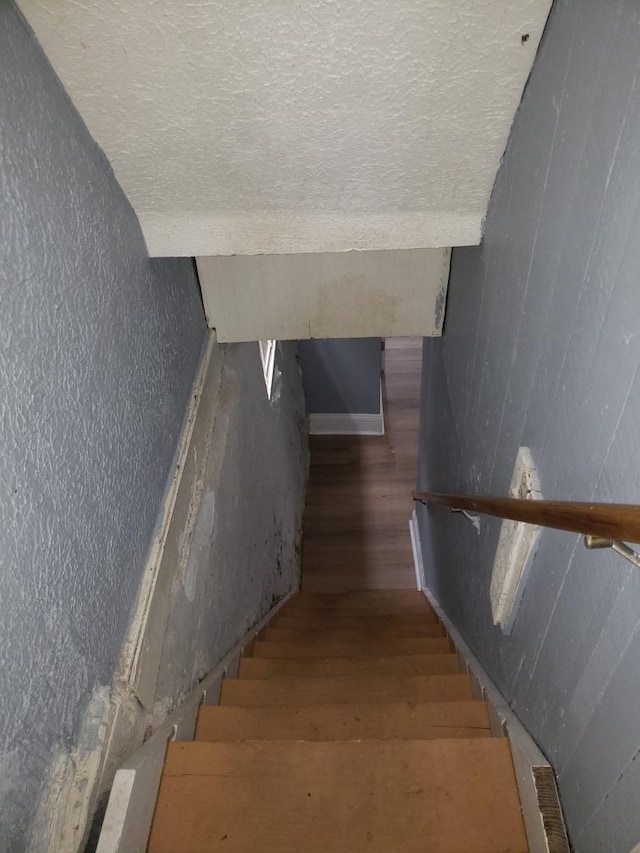 staircase with wood finished floors and a textured wall