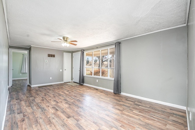 spare room with a textured ceiling, wood finished floors, baseboards, and ornamental molding