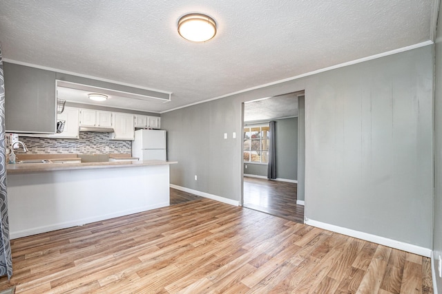 kitchen with a peninsula, light wood-style flooring, freestanding refrigerator, ornamental molding, and under cabinet range hood