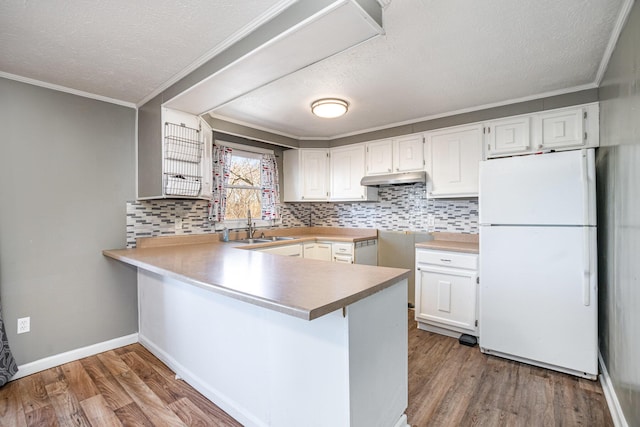 kitchen with wood finished floors, a peninsula, freestanding refrigerator, a sink, and under cabinet range hood