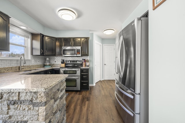 kitchen with a sink, backsplash, dark wood-style floors, stainless steel appliances, and light stone countertops