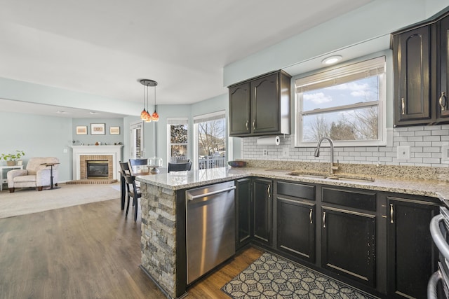 kitchen with a sink, tasteful backsplash, stainless steel dishwasher, dark wood-style floors, and a brick fireplace