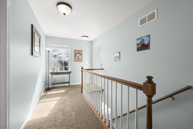 hall featuring an upstairs landing, visible vents, baseboards, and carpet floors