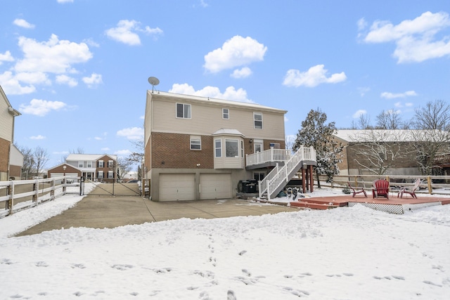 snow covered back of property with fence, stairs, a garage, a deck, and a gate