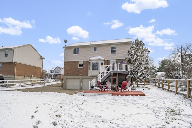 snow covered property with brick siding, a fire pit, a wooden deck, a fenced backyard, and an attached garage