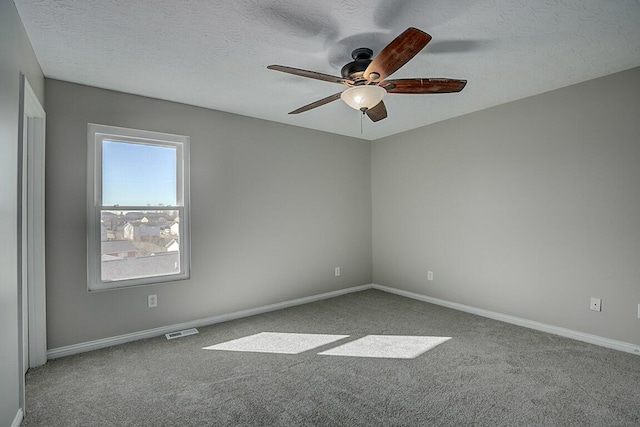 empty room with visible vents, a textured ceiling, carpet flooring, and a ceiling fan