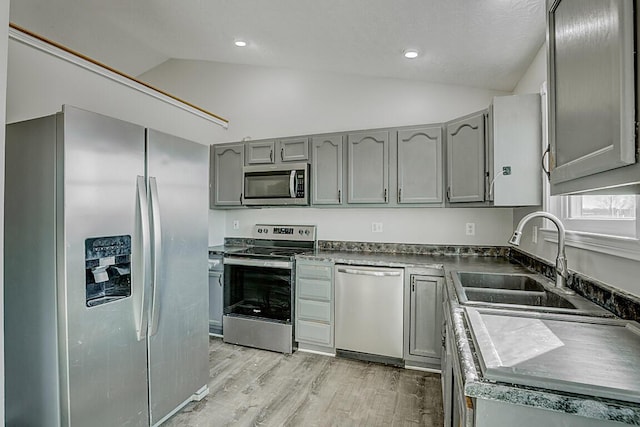 kitchen featuring lofted ceiling, gray cabinets, a sink, appliances with stainless steel finishes, and dark countertops