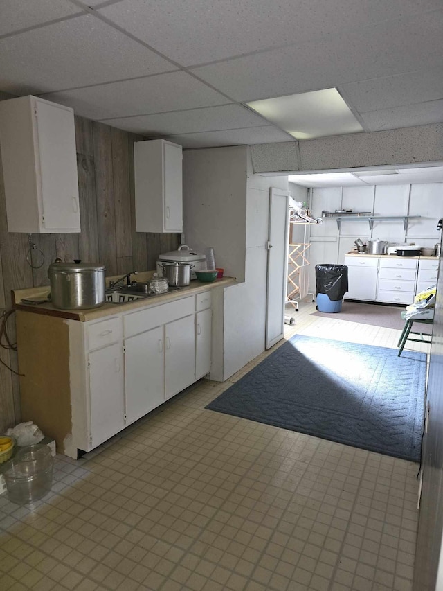 kitchen with light floors, white cabinetry, a paneled ceiling, and a sink