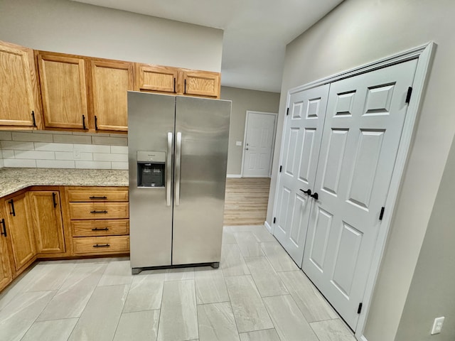 kitchen with decorative backsplash, brown cabinetry, light stone counters, and stainless steel fridge with ice dispenser