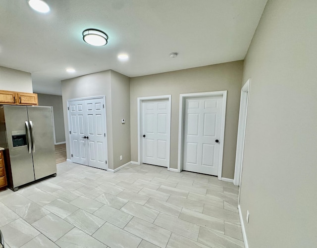 kitchen featuring recessed lighting, baseboards, stainless steel fridge, and brown cabinets