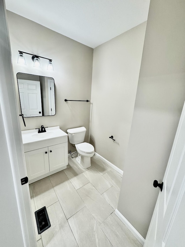 half bathroom featuring vanity, toilet, and baseboards