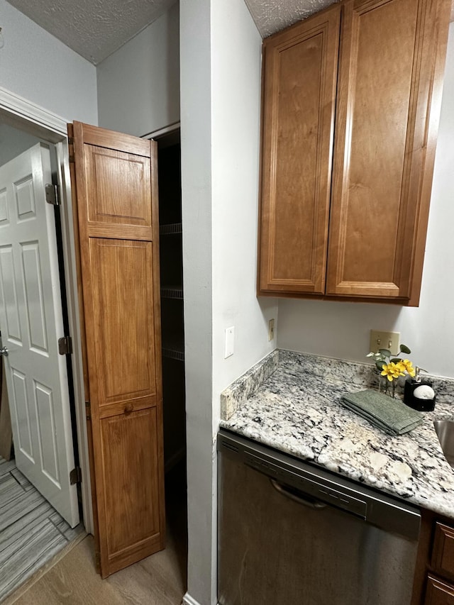 kitchen featuring stainless steel dishwasher, light stone counters, brown cabinets, and a textured ceiling