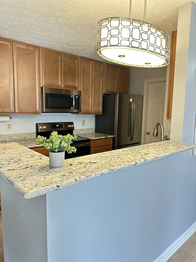 kitchen featuring light stone counters, brown cabinets, a peninsula, stainless steel appliances, and a textured ceiling