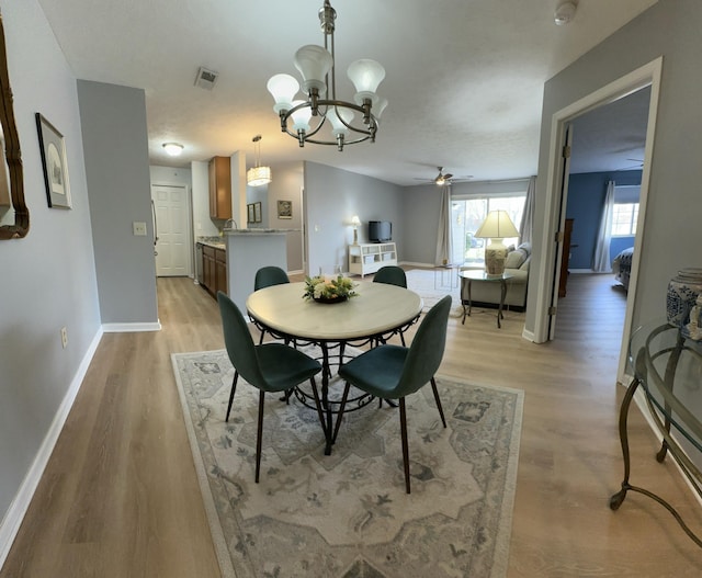 dining space featuring light wood-style flooring, ceiling fan with notable chandelier, visible vents, and baseboards