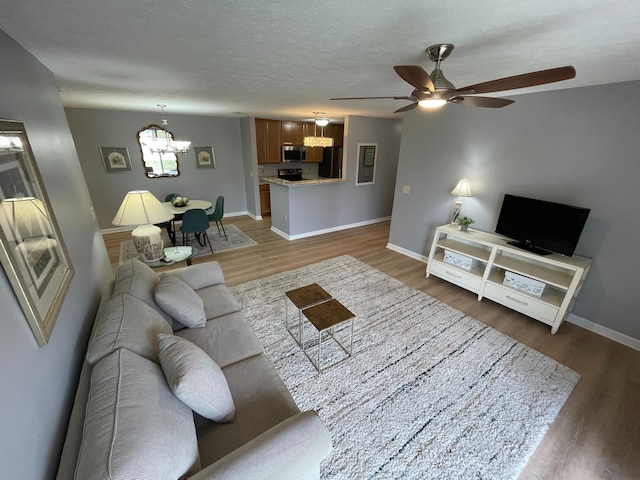 living room featuring ceiling fan with notable chandelier, a textured ceiling, baseboards, and wood finished floors