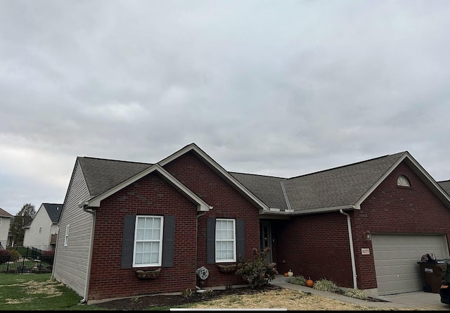 ranch-style home with a garage, brick siding, a shingled roof, and fence