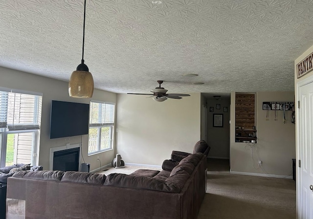 carpeted living room with a glass covered fireplace, a ceiling fan, baseboards, and a textured ceiling